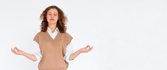 Curly beauiful young female makes mudra sign, relaxes after hard working day, keeps eyes shut,...