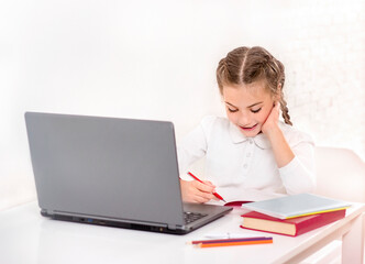 Schoolgirl learns at the table in front of the laptop