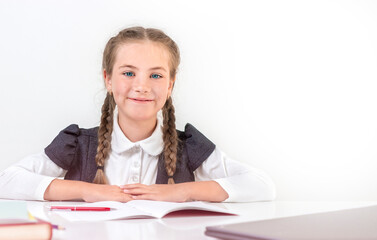 Schoolgirl sits behind a school desk and smiling on a white background