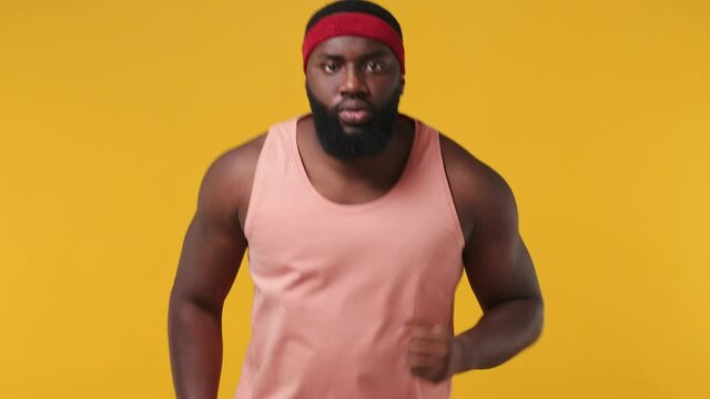 Serious fitness trainer instructor sporty young african american man sportsman 20s in headband pink tank top warm up train run kiss his biceps in home gym isolated on plain yellow background studio