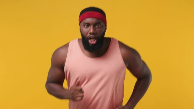 Happy fun fitness trainer instructor sporty young bearded african american man sportsman 20s in headband pink tank top warm up training running in home gym isolated on plain yellow background studio