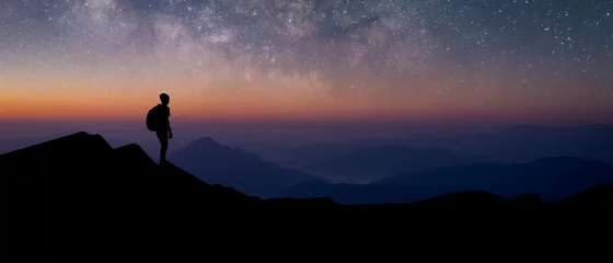 Poster Panorama silhouette of young traveler with backpack standing and watched the star and milky way alone on top of the mountain. He enjoyed traveling and was successful when he reached the summit. © Tarokmew