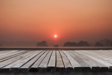 Fototapeta na wymiar Empty old wooden table in front of blurred background of the sea and sunrise over island background. Can be used for display or montage for show your products.