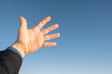 Human hand holding snow on blue sky background. Melting snowflakes on the male palm, illuminated sunshine. Copy space