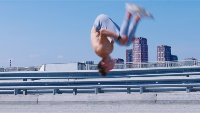 Guy with naked torso doing backflip four times on embankment. Male gymnast, acrobat practising salto backward on city river esplanade. Sportsman training outdoor. Young man does sport outdoor