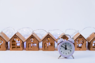 Lovely wooden houses, Christmas garlands, stand in a row. The clock is in the foreground. The concept of the timely acquisition of real estate