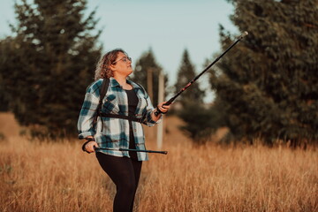 A woman with sticks, a backpack on her back, and mountaineering equipment walking on top of a mountain at sunset.