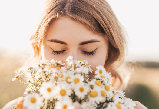 Young beautiful girl with a bouquet of daisies in a wheat field