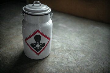A white metal can with a poisonous liquid on a wooden table. A warning sticker about toxic fluid in...