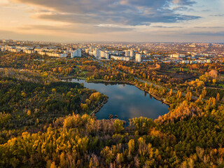 Fototapeta premium Aerial view of a lake in a park with autumn trees. Kishinev, Moldova. Epic aerial flight over water. Colorful autumn trees in the daytime.