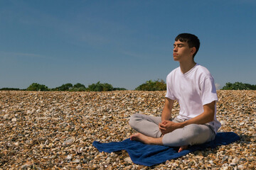 Fototapeta na wymiar A Caucasian teenage boy meditating on a stony beach with his hands resting on his lap