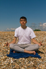 Fototapeta na wymiar A Caucasian teenage boy meditating on a stony beach with his hands in the Shuni position