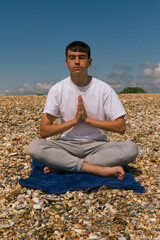 Fototapeta na wymiar A Caucasian teenage boy meditating on a stony beach with his hands in a prayer position