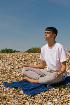 A Caucasian teenage boy meditating on a stony beach with his hands in the Shuni position