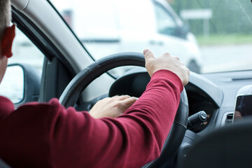  Man in a red sweater is driving a car. Hands on the wheel