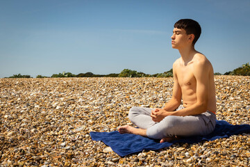 Naklejka na ściany i meble Teenage boy on a beach meditating