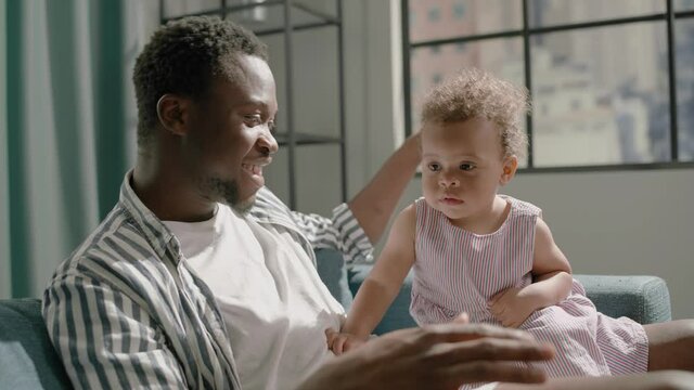 Young black man plays patty-cake with toddler daughter