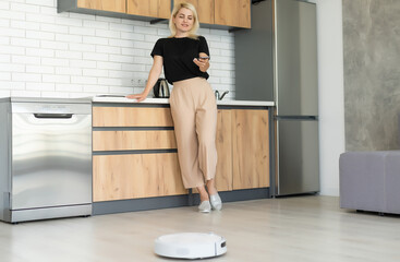 Young woman using automatic vacuum cleaner to clean the floor, controling machine housework robot