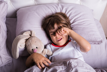 a small child in pajamas wakes up on a bed with stuffed toy
