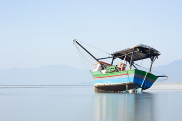 Obraz premium Long exposure of a wooden fishing boat stranded on the beach in a shine day 