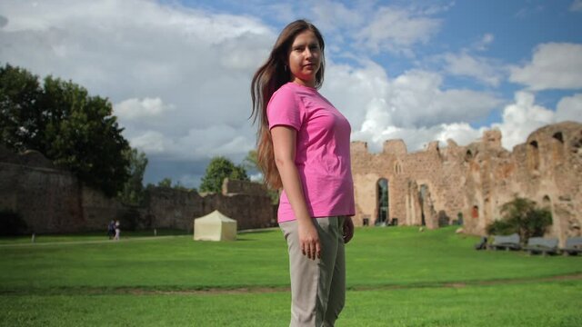 A young authentic woman in a pink T-shirt and gray pants poses
