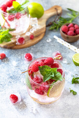 Hard seltzer cocktail with raspberries and lime on a gray stone table top.