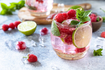 Hard seltzer cocktail with raspberries and lime on a gray stone table top.
