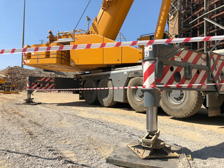 Outriggers of heavy all-terrain mobile crane at construction site. Crane work execution area fenced...