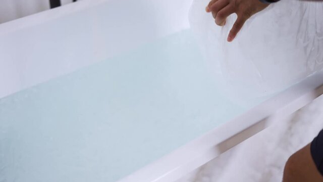 Man filling bath with ice cubes, close up