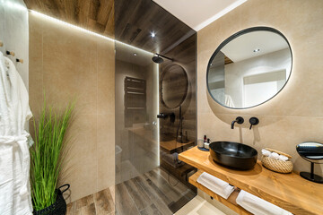Modern tiled bathroom in beige and brown warm colors.  It has shower cabin with glass partition,...