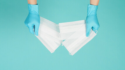 Hands holding face masks wear blue medical gloves on mint green or Tiffany Blue background.