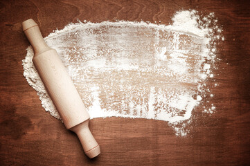 Roller pin and white flour on a dark wooden brown background. Free space for text. View from above. 