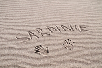 Inscription Sardinia in the sand with the imprint of two hands