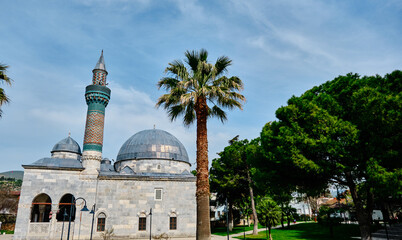 Fototapeta na wymiar Green mosque (yesil camii) in Nicaea (iznik) during spring and sunny day in center of the city covered by many green plants, and palm trees and it turquoise color minaret