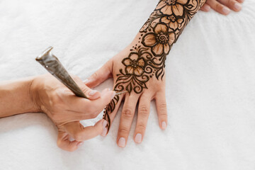 Top view art henna tattoo on woman hands. master artist drawing Arabic mehndi for bride before...