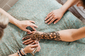 Mehndi artist drawing floral henna tattoo on woman hand in beauty salon. Master applying...