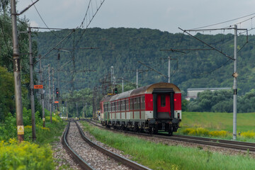 Fototapeta premium Passenger train with red electric locomotive and passenger coaches in summer