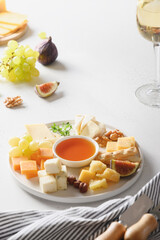 Cheese platter with grapes, nuts, figs on a white background. Vertical format. Festive gourmet snack.