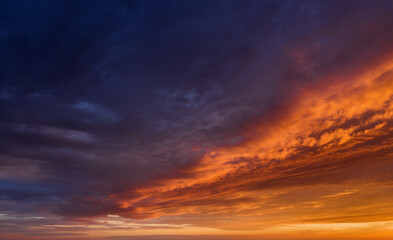 Naklejka na ściany i meble Vibrant sunset sky with dark clouds illuminated by orange sunlight