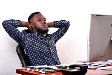 young business man sitting at desk holding his hands behind his head.