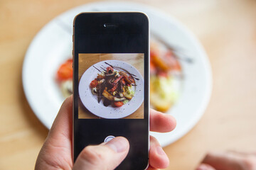 A man photographs a delicious salad on his phone in a restaurant