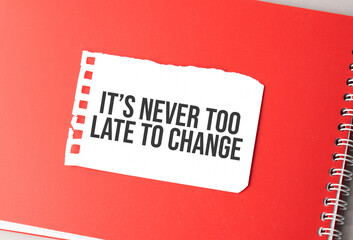 The word It is never too late to change on torn paper on red notepad,.