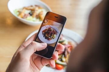 A man photographs a delicious salad on his phone in a restaurant