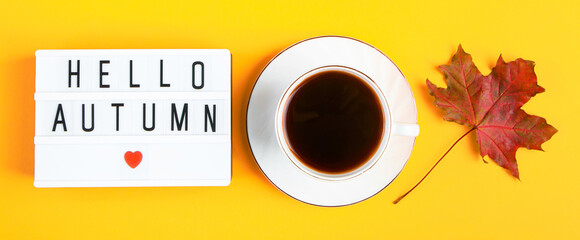 Hello autumn concept. Cup of coffee and sign with  inscription on yellow  background. Fallen leaves and hot drink.