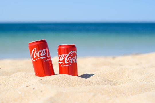 Anapa, Russia - July 2021: Two red cans of Coca-Cola stand buried in the sand on the beach.