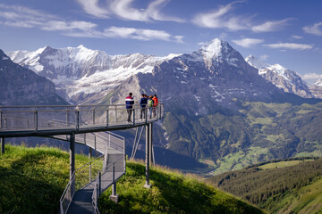 des touristes sur une passerelle dans le vide devant un panorama des alpes 