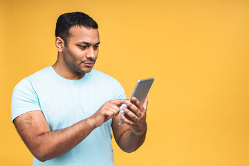 Using tablet. Happy winner! Young handsome african american indian man smiling holding tablet and playing games or using a booking app isolated over yellow background.