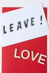 the expression "leave!" stencilled in black on white paper, with the word "love" in plain wood letters on a red background