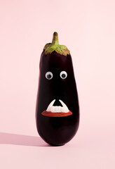 Vampire face made of eggplant, eyes and teeth against pastel pink background. Creative Halloween...