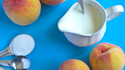 Milk Pitcher Surrounded by Fresh Peaches and Measuring Spoons on a Blue Background | Peaches and Milk
